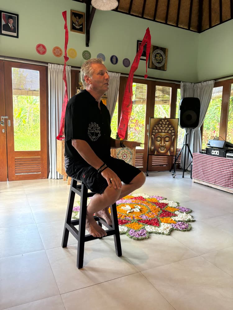 Ole Dammegard speaking to the group from a stool in the open lecture hall, a flower mandala laid on the floor