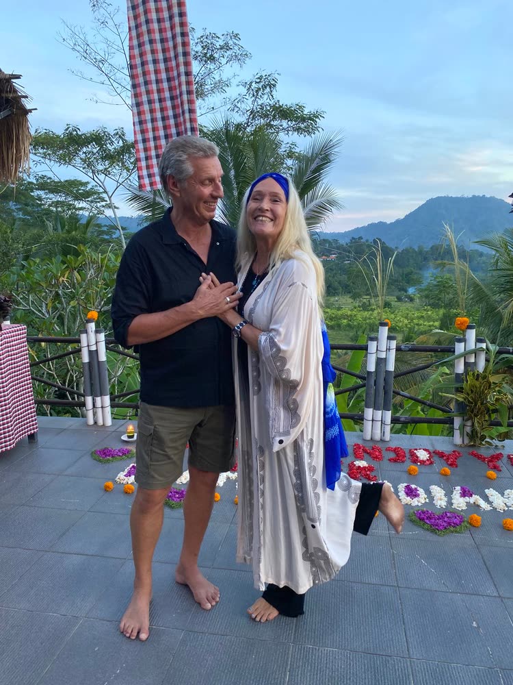 Two retreat guests laughing together on the terrace at dusk, flower petals spelling a greeting on the tiles