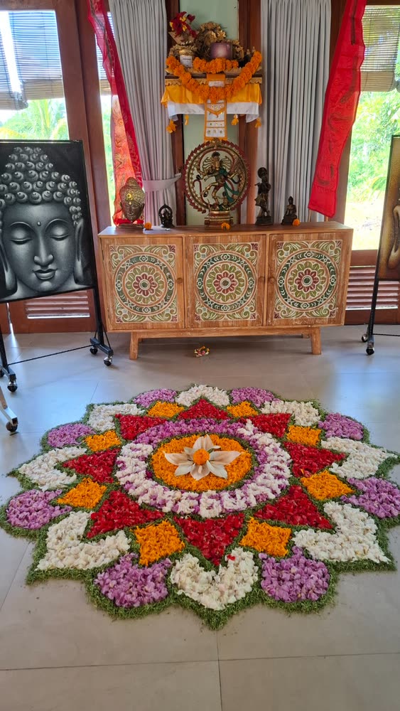 A large mandala of fresh flowers laid on the floor of the meditation hall beneath a Balinese altar