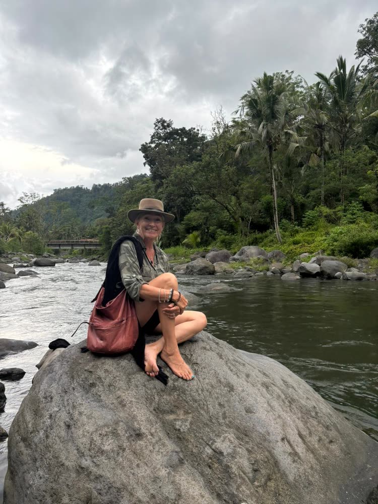 A retreat guest resting on a boulder in the river, palms and jungle behind