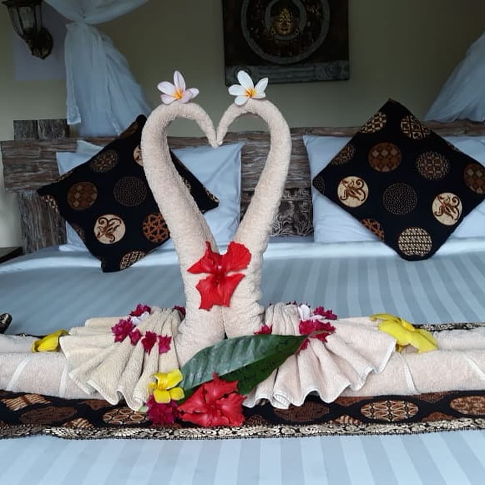 Retreat bed dressed with towel swans, frangipani and hibiscus flowers among batik cushions