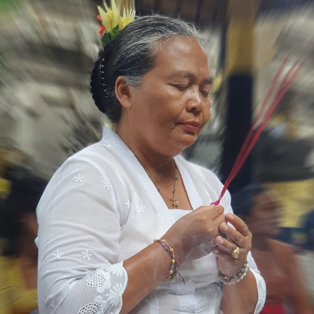 Balinese woman in white ceremonial dress praying with incense during a temple ceremony
