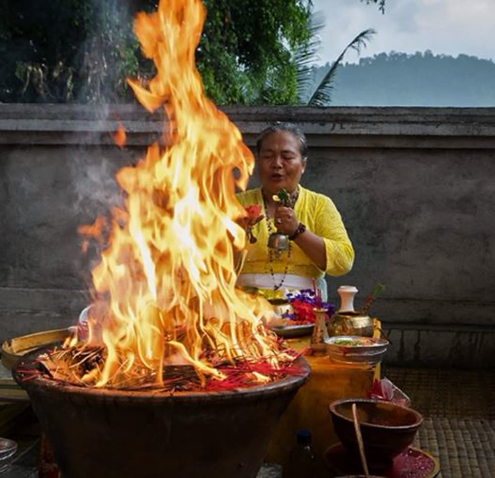 Balinese priestess tending a tall flame during a fire purification ceremony at the retreat