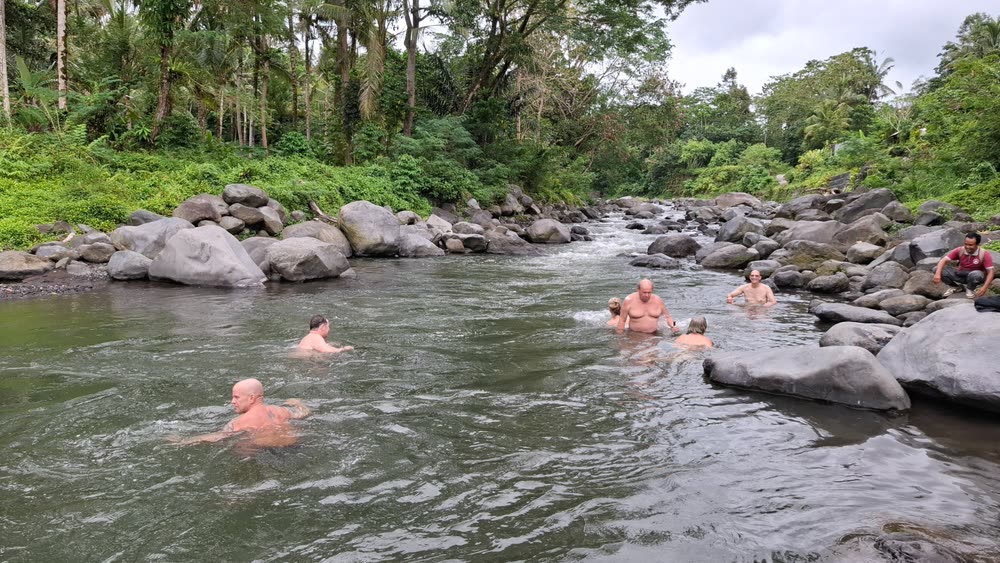 Retreat guests bathing in the river among the boulders below the jungle